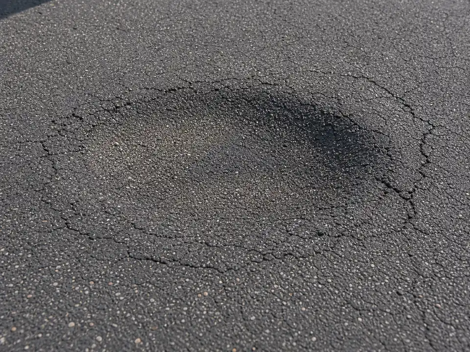 Close-up of a settled asphalt driveway depression with cracked edges