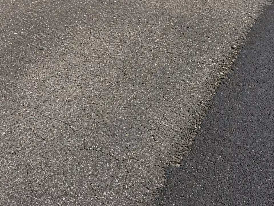 Weathered asphalt texture with fading, fine cracks, and raveling